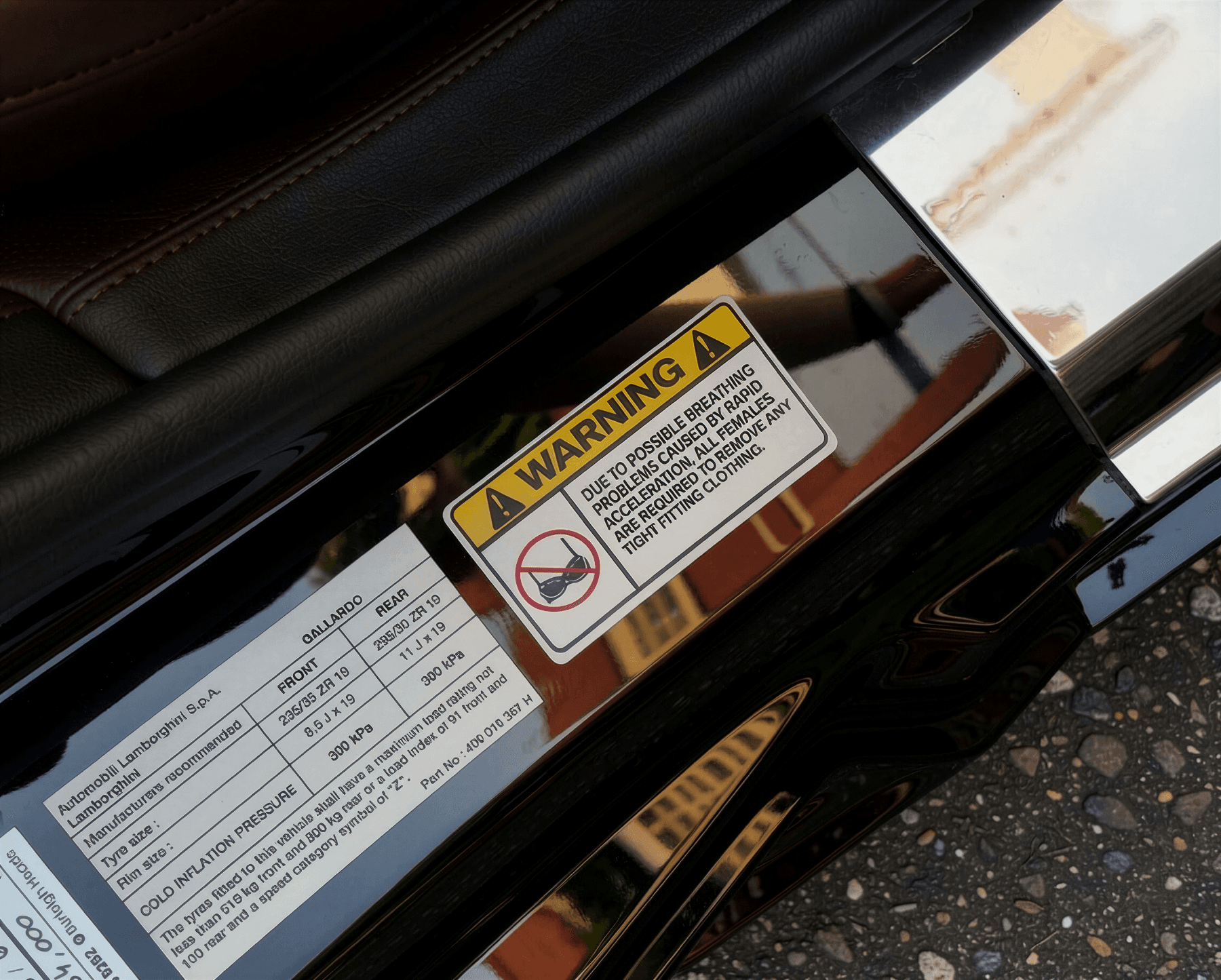 Warning label applied to the door jamb of a black sports car, beside the factory tyre pressure placard